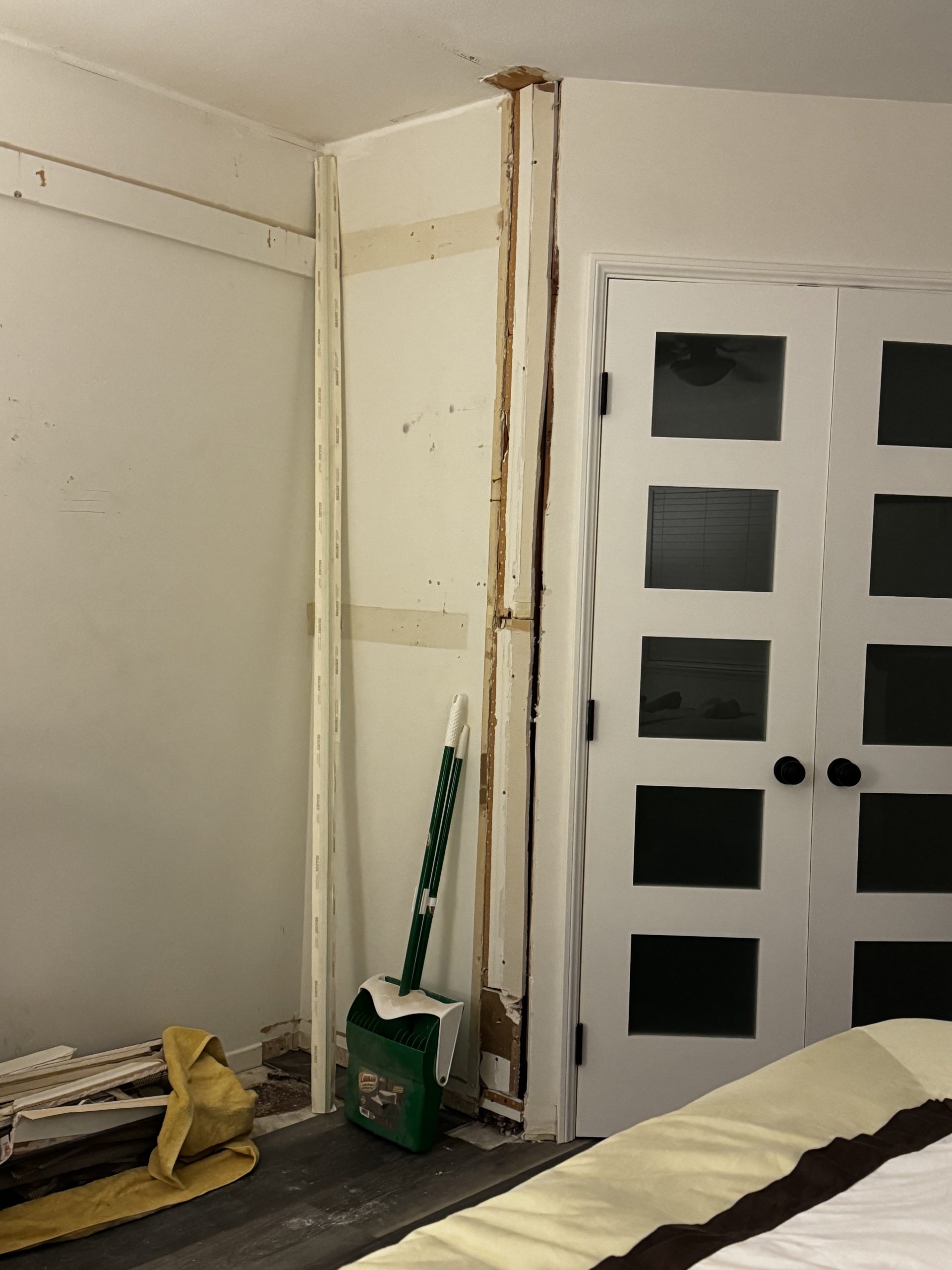 An unfinished closet installation stands beside white French doors, with exposed framing, tools on the floor, and patchy drywall around the opening.