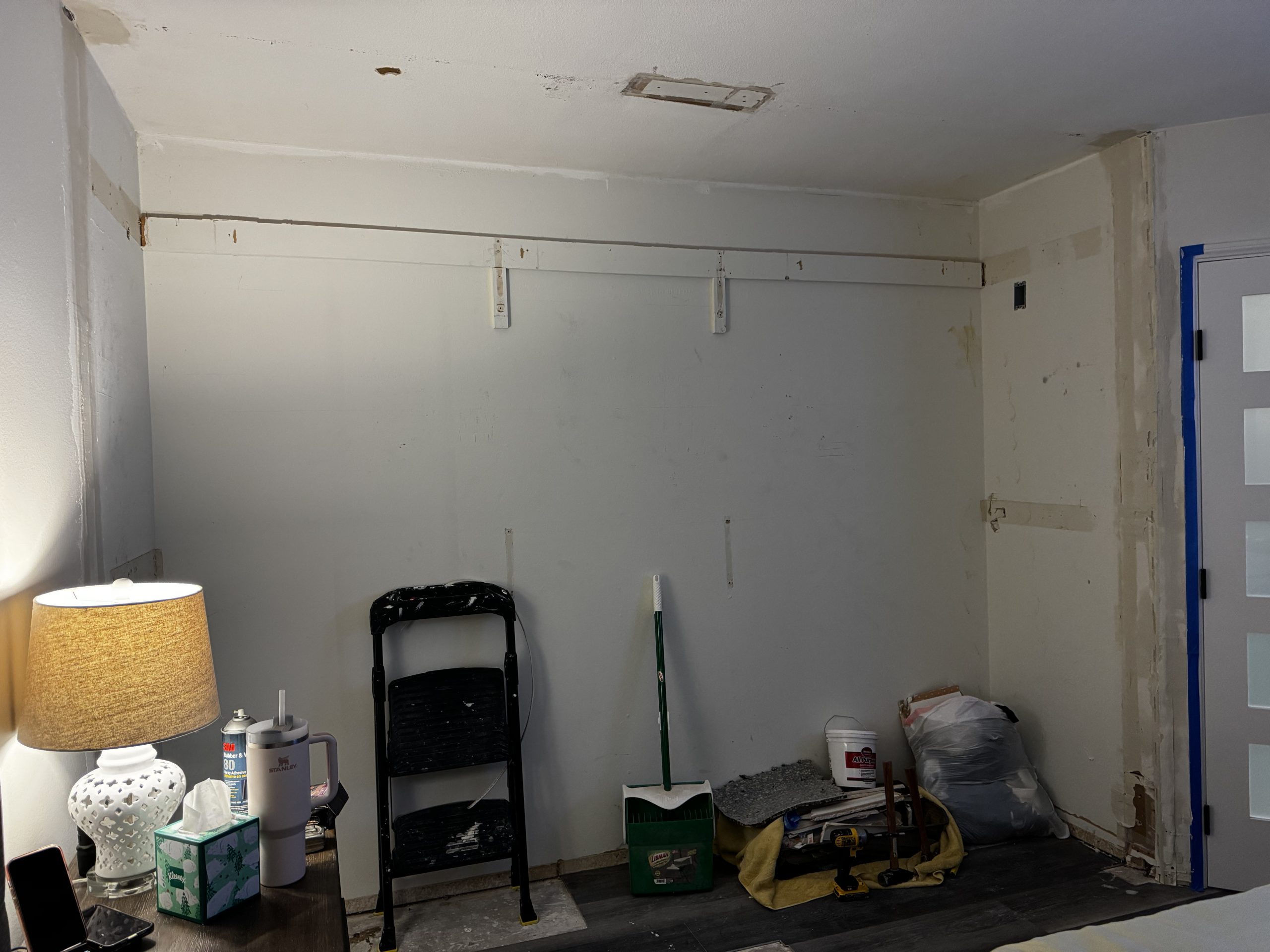 An unfinished closet wall shows mounting rails, patchy paint, and scattered tools and supplies on the floor during a remodeling job.