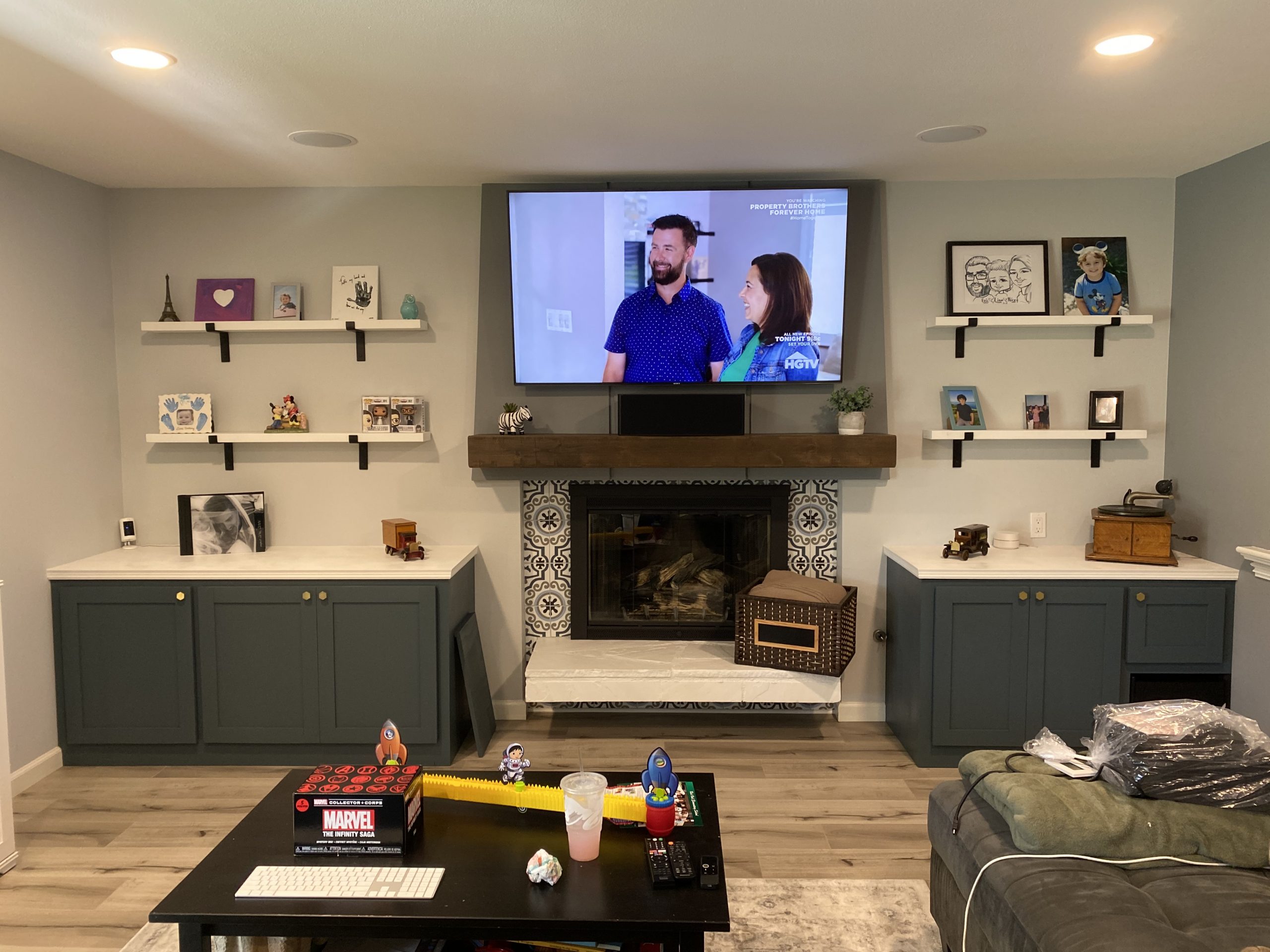Mounted television sits above a fireplace with built-in shelving, cabinets, and framed family photos in a bright remodeled living room.